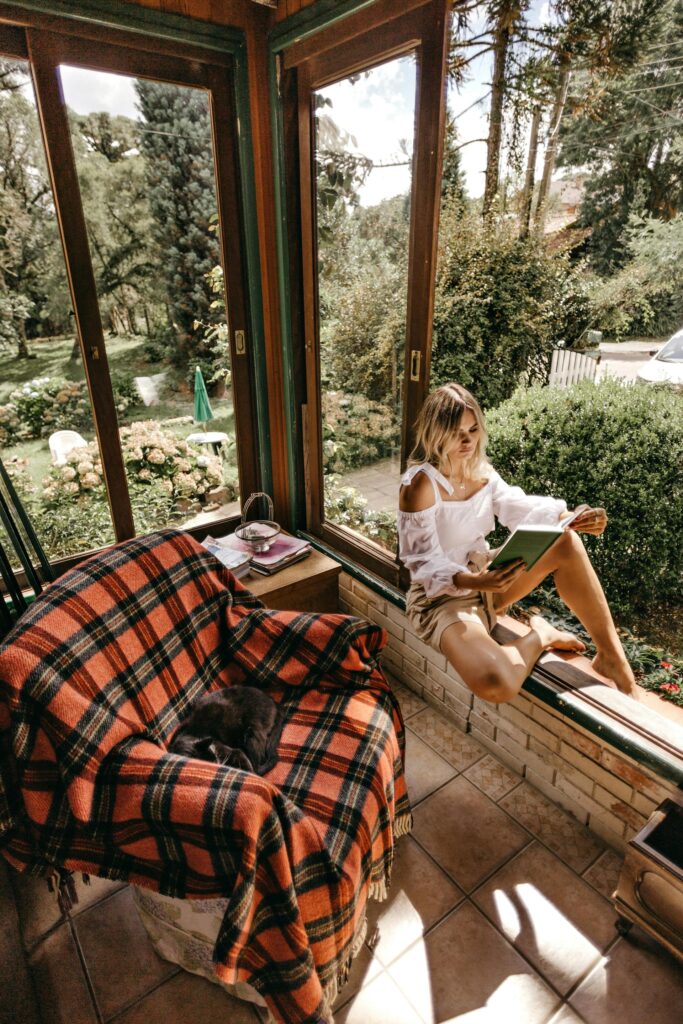 woman sitting on window seal reading a book enjoying stress relief in the sun