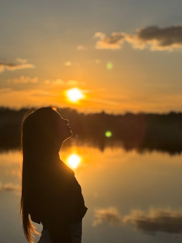 Silhouette of girl standing in front of lake as the sun rises.